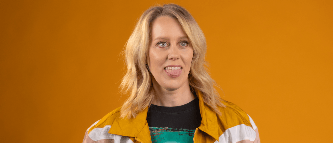Claire has short blonde wavy hair. She is wearing a colourful jacket that is yellow, white and pink over a graphic t-shirt. She is looking off camera and poking out her tongue. The background is a mustard colour. 