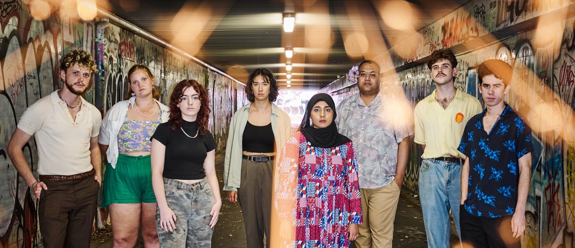 Eight Young People are standing in a tunnel with serious faces, there are sparklers in front of the cameras. 