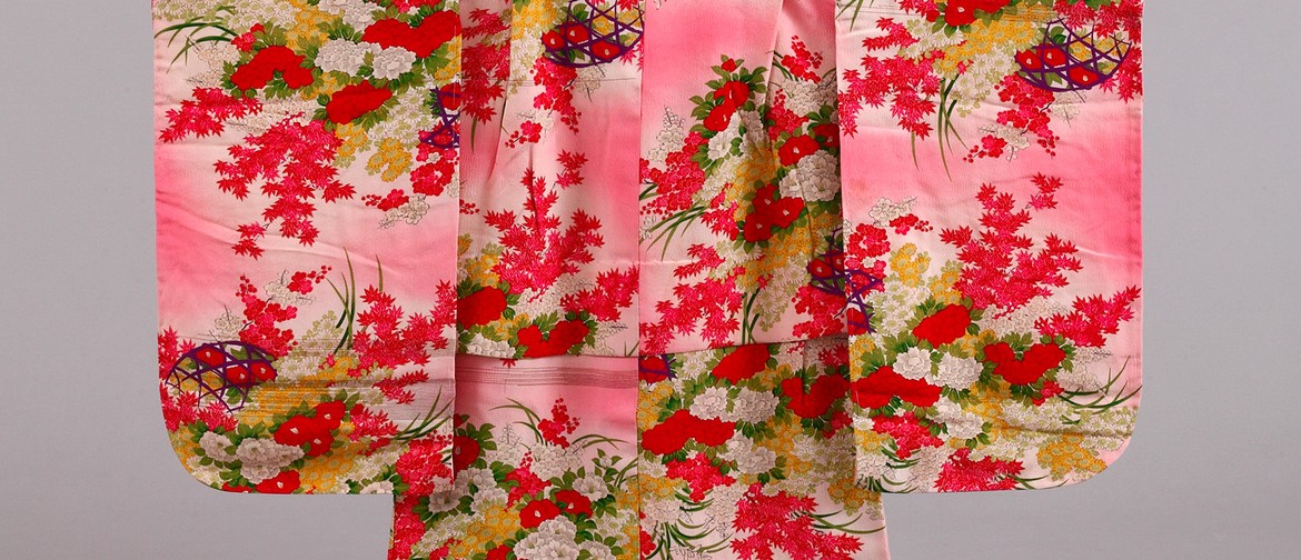 A photograph of a section of a children's kimono (Japanese traditional garment, sunset pink and decorated with various flowers arrangements in red, mustard, and white