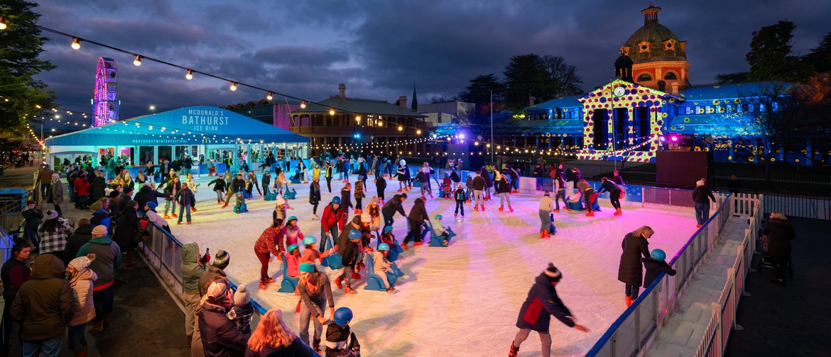 Bathurst Winter Festival Ice rink full of people ice skating at night at the Bathurst Winter Festival with the the illuminated Bathurst Courthouse and Ferris wheel in the background.