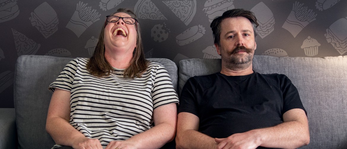 A couple sitting on a couch. The woman is laughing maniacally. The man looks sad.