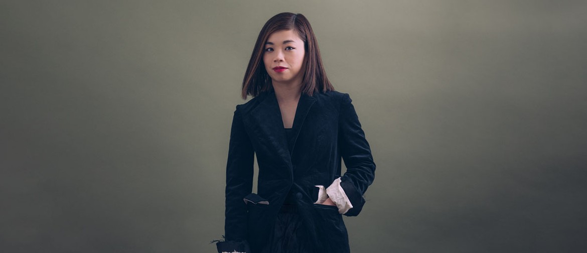 Open Rehearsal with Elim Chan A portrait of Elim Chan, standing with one hand in their pocket and the other holding a baton