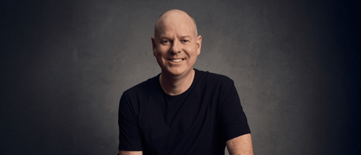 Comedian Tom Gleeson wearing a black tshirt in front of a black background, smiling
