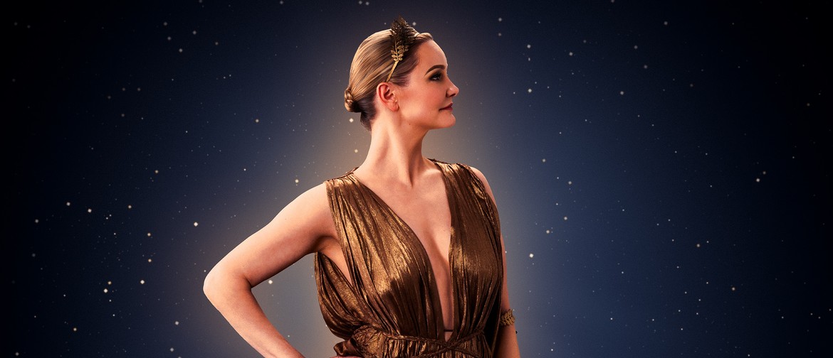 Isabella is dressed in a golden toga and is posing on profile wiht her hand on her hip.