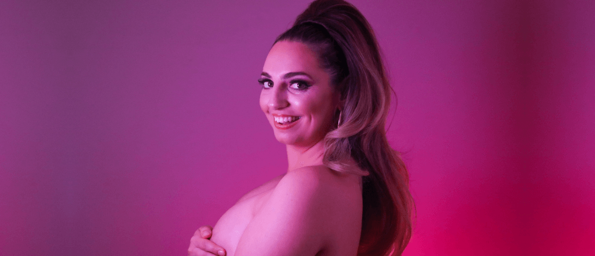 A topless woman with long brown hair covering her breasts and smiling at the camera