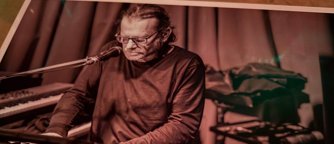 Bespectacled man playing keys with microphone, in sepia tone.