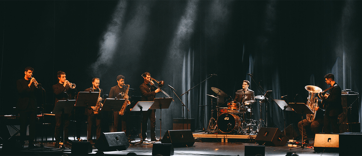 8 musicians play brass instruments, drums, and guitar on a stage