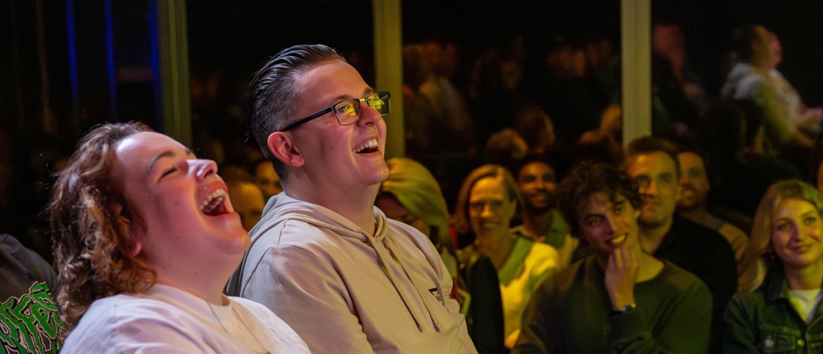 A man looking at his partner, smiling and sitting in the crowd at a comedy show. 